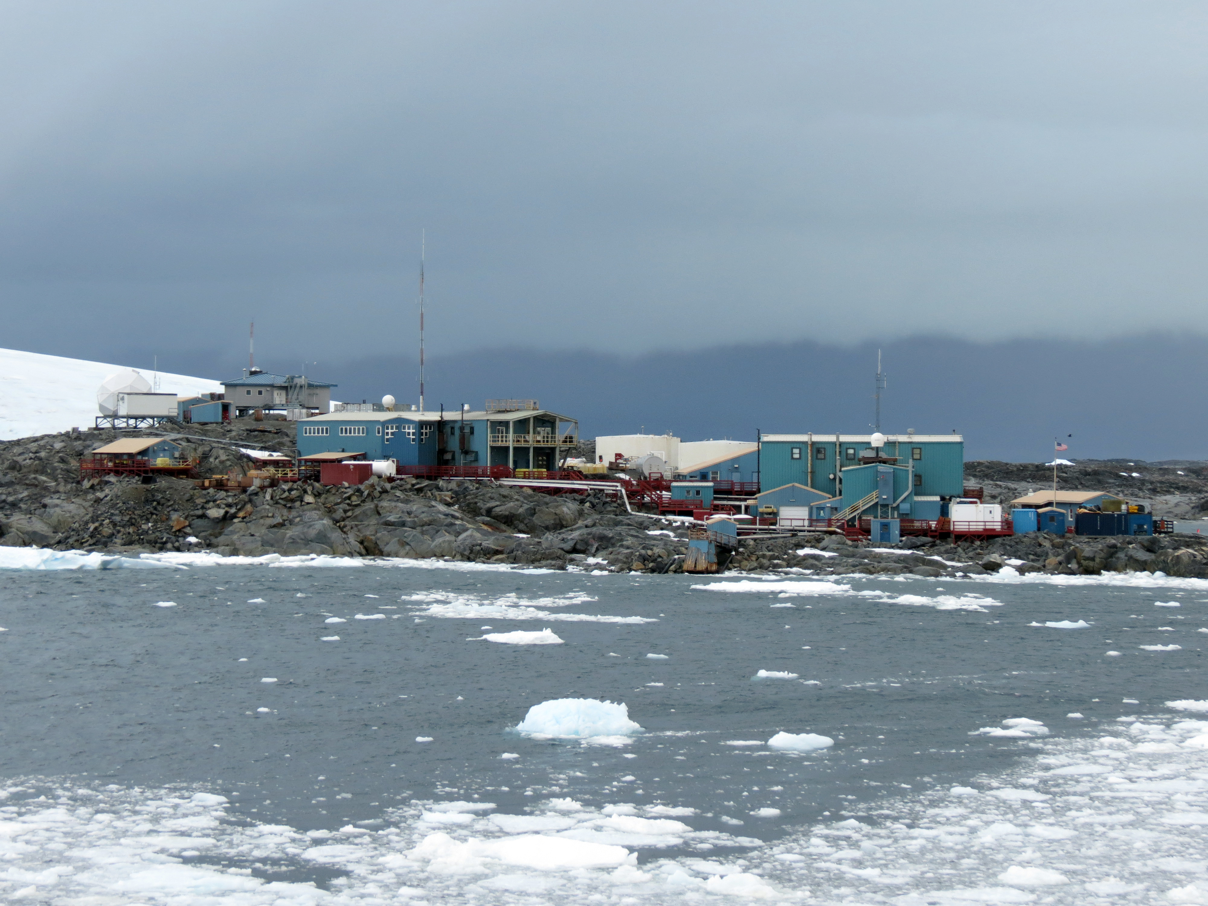 Palmer Station, Antarctica, a cluster of blue and tan buildings on a rocky point with brash ice in the foreground