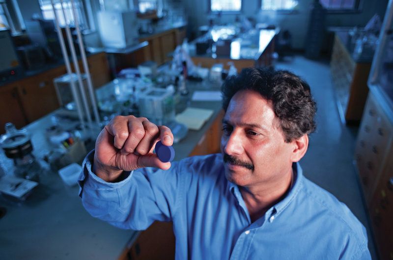 A man in a laboratory holds up a small blue disc between his fingers