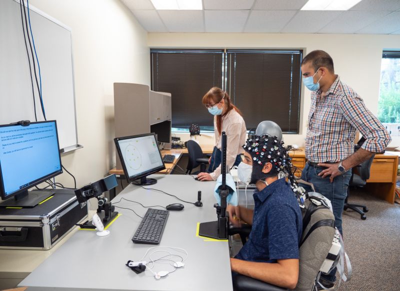 Researchers observing a student testing out AI-enabled learning equipment at a computer.