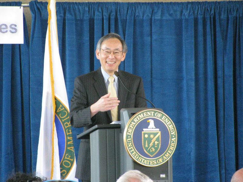 Steven Chu smiles while standing at a podium with a Department of Energy seal