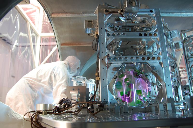 A worker in a white lab suit is pictured examining a large metal structure with wires