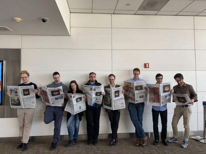 Team members of the Event Horizon Telescope hold up newspapers displaying the history-making black hole image on the front page.