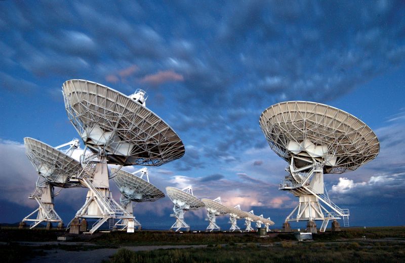 Clouds at twilight over a group of large radio dishes.