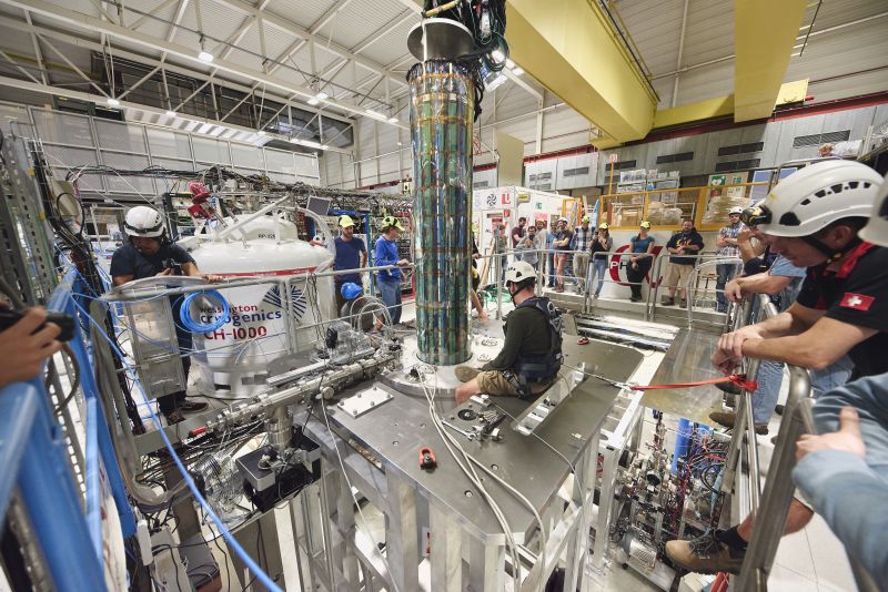 A cavernous laboratory filled with equipment and people watching from a raised platform.