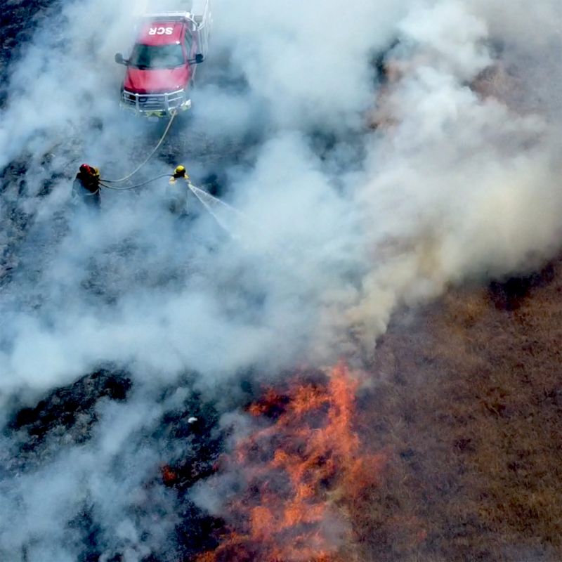 A drone image of a firefighter using a HEN nozzle to suppress a grass fire.