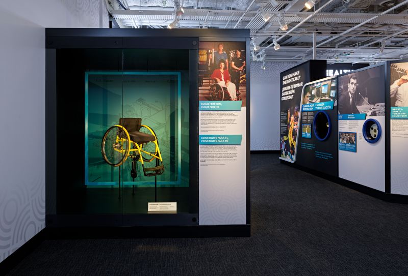 This image shows an artifact display from the bilingual Change Your Game/Canbia tu Jeugo exhibition, which opened at the Smithsonian Institution's National Museum of American History on March 15, 2024. The artifact is the Quickie sports wheelchair co-invented by Marilyn Hamilton and used by her to compete in the U.S. Open wheelchair tennis tournament in the 1980s.