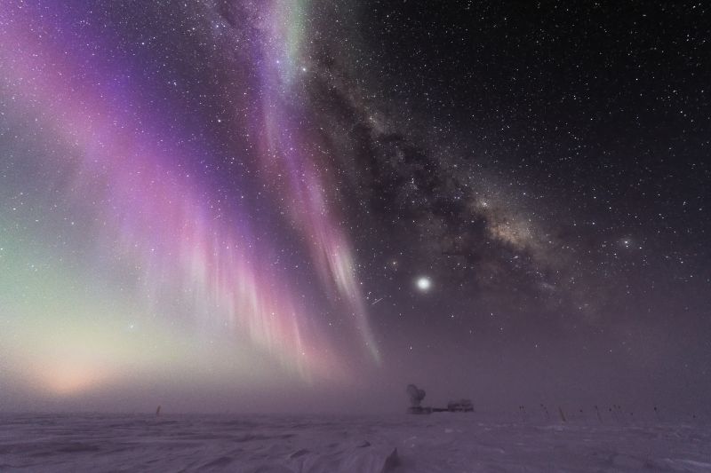 Purple auroral streaks in the night sky, with a building on the horizon.