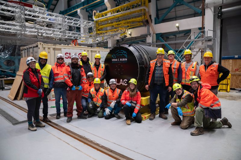 A group of people in hard hats standing near a large camera in a warehouse.