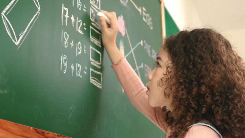 Young female student solving math equations at a chalkboard.