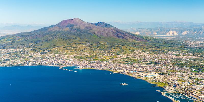 View from the sky of a city on the bay with a dormant volcano in the background.