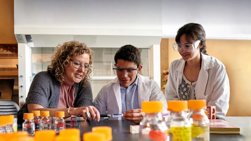 Three scientists wearing safety glasses in a lab with test bottles in the foreground
