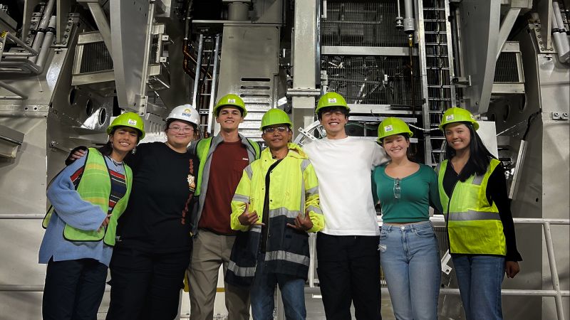 Group photo of students and mentors wearing hard hats in front of interior workings of the Inouye Solar Telescope facility