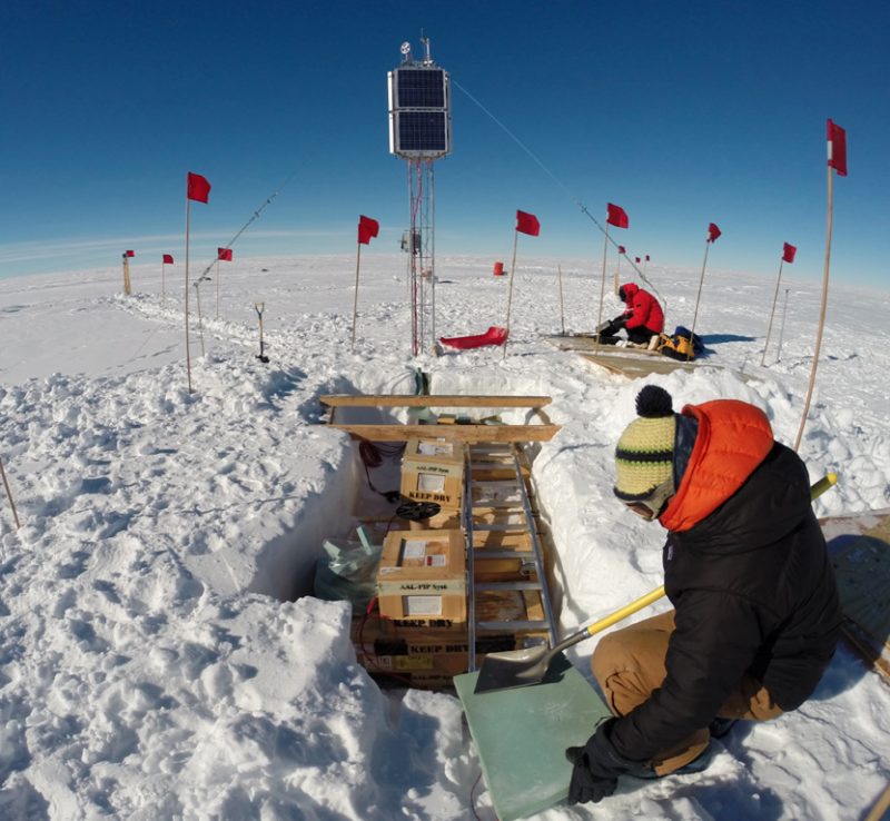 Researchers kneel down in the snow in Antartica to work on equipment.