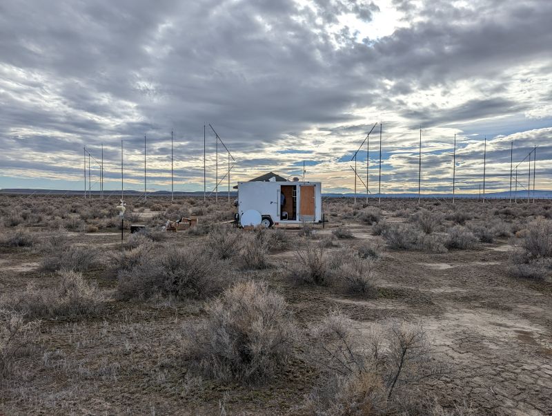 A white trailer with an open door in the middle of a dry field.