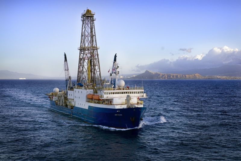 A large blue and white ship with a large steel tower sails through a dark ocean