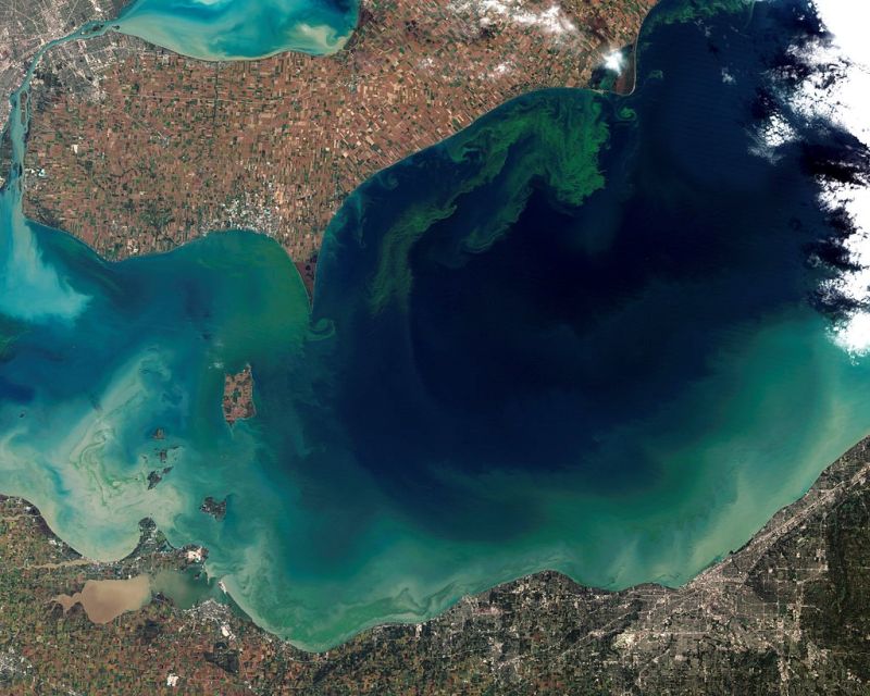 A satellite image shows a brown landscape surrounding a body of blue water with green swirls