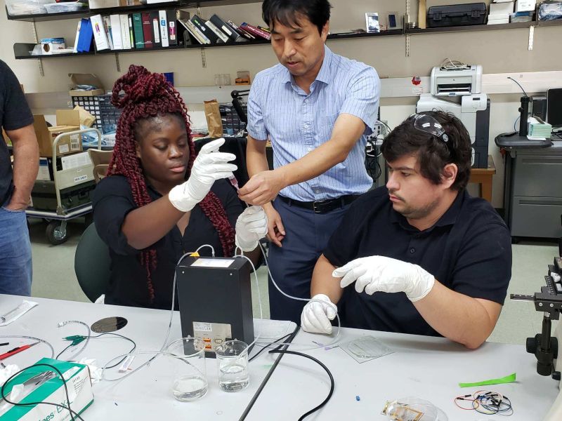 Three people at a lab bench working with tubes of fluid.
