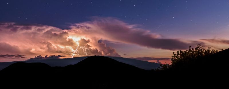 A deep blue night sky with lightning coming down from bright clouds.