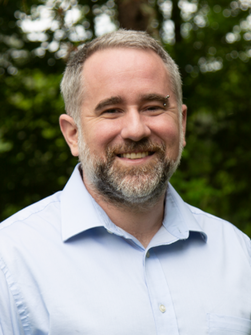 portrait of man with salt and pepper hair and beard wearing a button up collared shirt