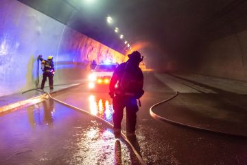 Firefighters responding to a car accident in a tunnel with a police car in the background.