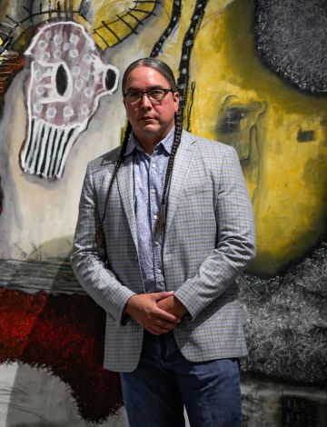 Photo of Dr. Sean Chandler, an American Indian scientist standing in front of a tribal nations mural.