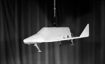 Space vehicle model hanging in mid-air against a dark background.