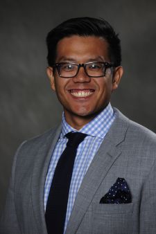 A man in a suit and tie and glasses is smiling