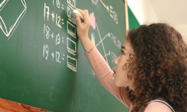 Young female student solving math equations at a chalkboard.