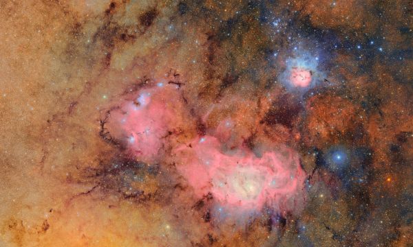 Against a background dense with glowing orange and golden stars, two nebulas appear as pinkish clouds of gas and dust.