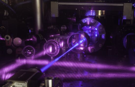 Purple laser beams emitted out of metal devices crossing each other in the dark.