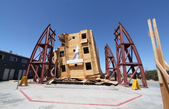 A wooden building shows damage after testing on a giant shake table.