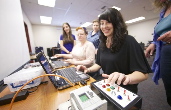 A woman stands at a laptop pressing buttons on a control panel