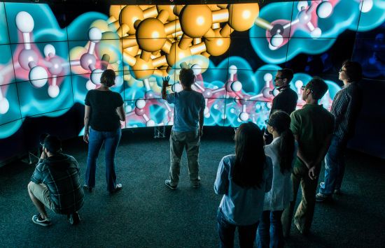 A researcher at the Electronic Visualization Laboratory discusses a visualization of a balls-and-sticks model of a molecular chemistry dataset on the CAVE2 System with students.