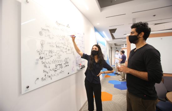 Two researchers stand at a white board that is covered in equations
