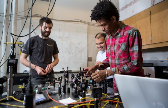Three researchers stand around a work bench covered in research equipment