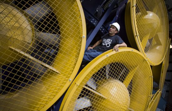 A man wears a hard hat while standing among giant, person-sized fans