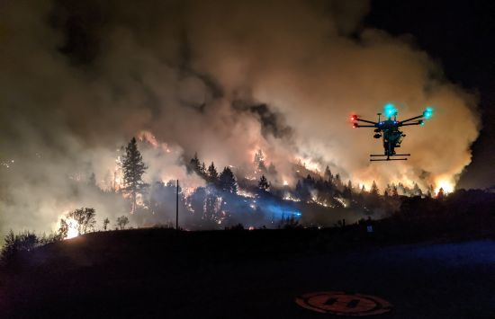 A drone hovers over its flight pad on the perimeter of a prescribed burn