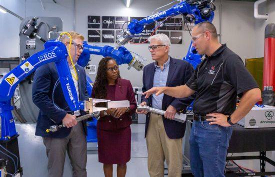 A group of people stand in a lab surrounded by robotic arms