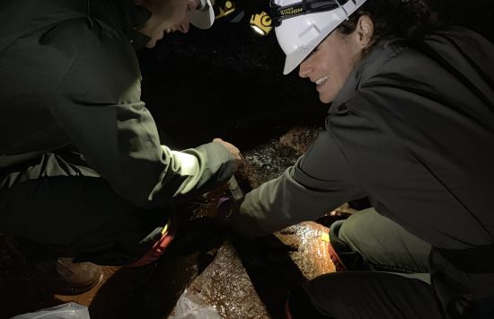 Two smiling researchers wearing hard hats in an underground tunnel.