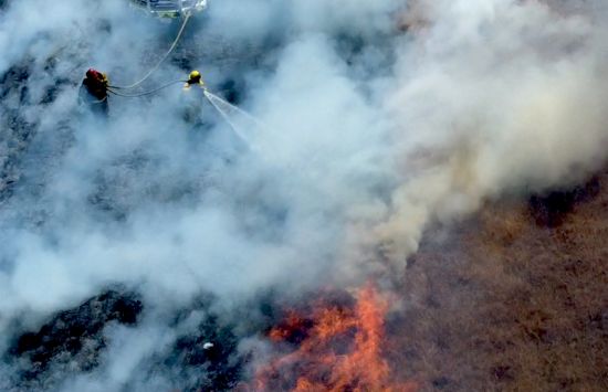 A drone image of a firefighter using a HEN nozzle to suppress a grass fire.