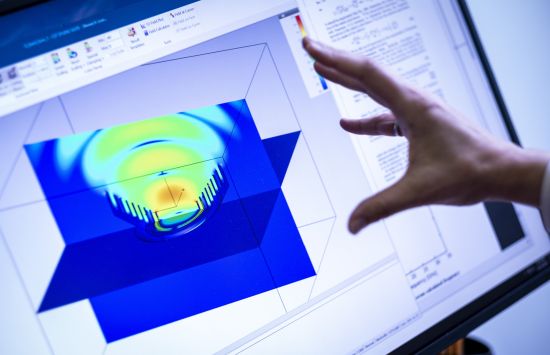 An open hand facing a computer screen showing an abstract blue and green image.