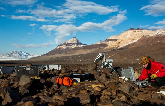 The photo shows a scientist adjusting equipment in Antarctica.