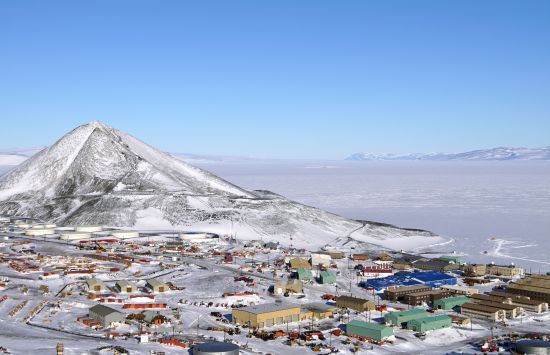 Clustered buildings in the snow at the base of a hill.