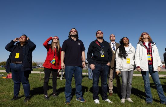 People standing in a field, wearing eclipse sunglasses and viewing a solar eclipse.