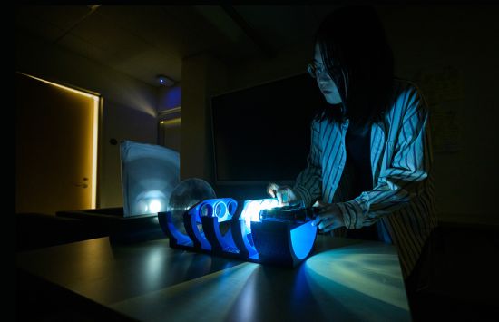 A research assistant in a dark room working on an illuminated device.