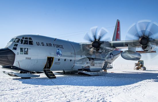 A plane with propellors running, sitting on a snowy runway.