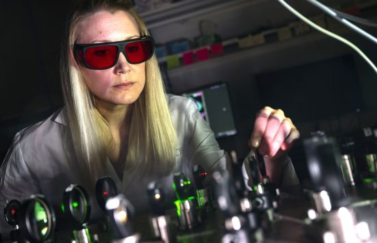 A researcher wearing protective goggles adjusts an imaging device.