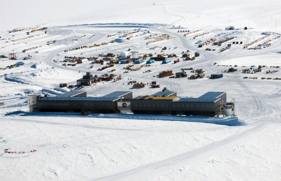 Aerial view of an icy scene with a large building in the foreground and clustered smaller buildings beyond.