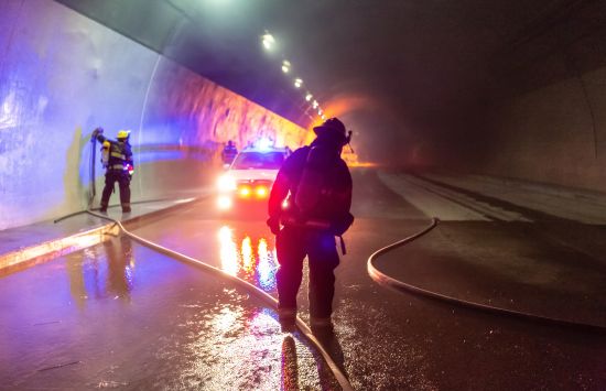 Firefighters responding to a car accident in a tunnel with a police car in the background.