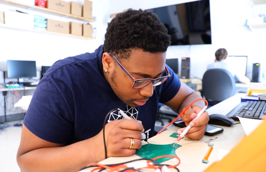 A student holds leads up to a sensor on a lab bench.